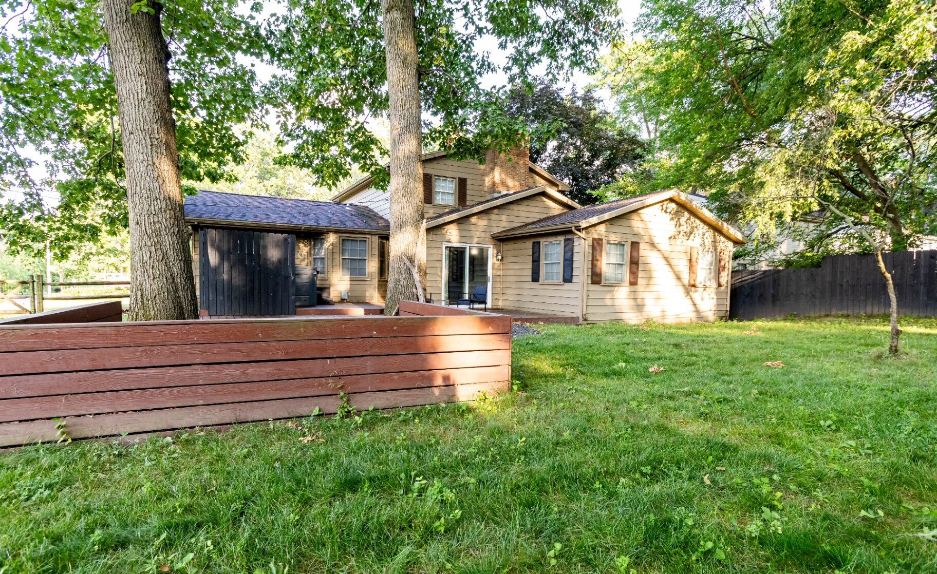 Backyard view of the home with shaded trees and a spacious green lawn