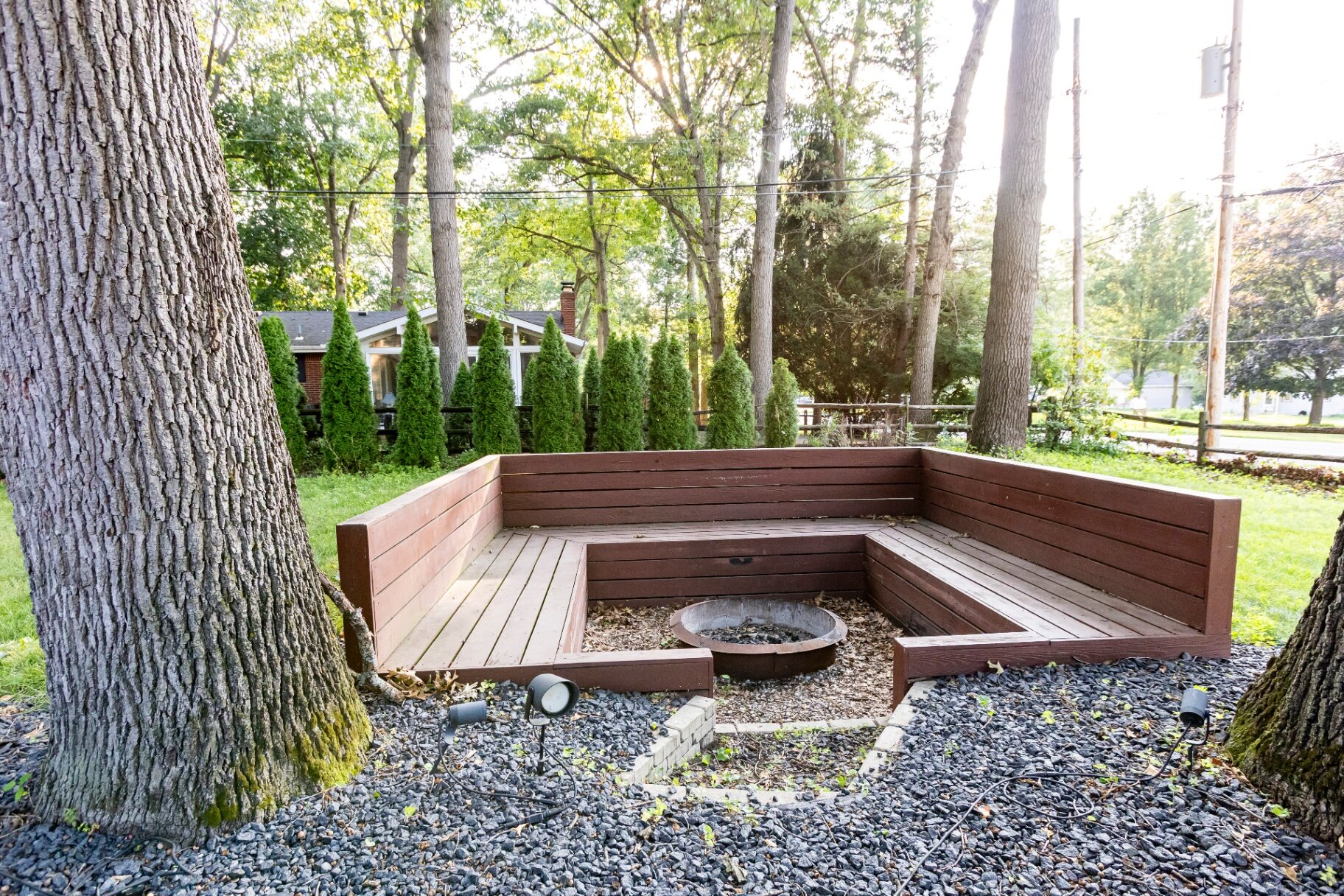 Backyard fire pit with built-in wooden bench seating surrounded by trees